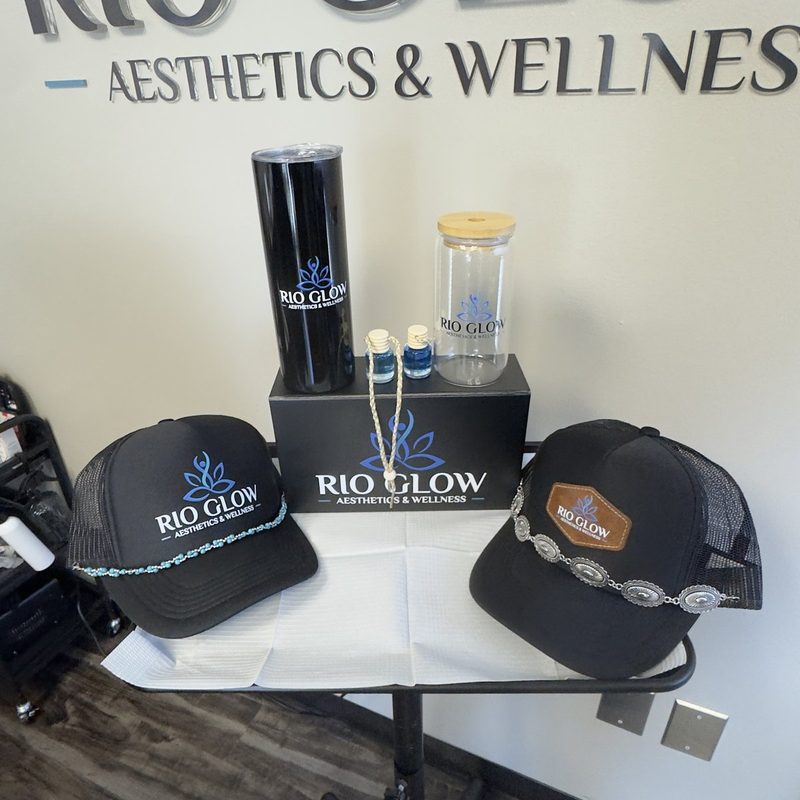Two branded trucker hats, a tumbler, a glass and a gift box on display at a med spa