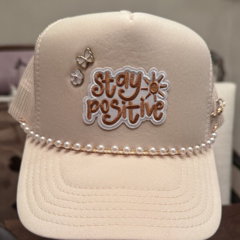 Cream trucker hat, shown whole, with a stitched patch, pins and a pearl chain