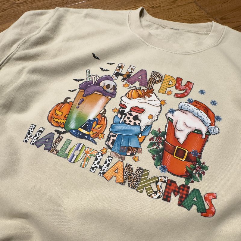 Sand crewneck with a full-colour print of three holiday drinks for Halloween, Thanksgiving and Christmas